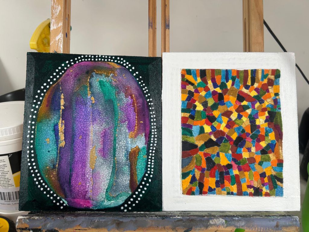Two paintings on an easel: a shimmering purple and teal oval framed with white dots, and a colourful mosaic of small painted shapes