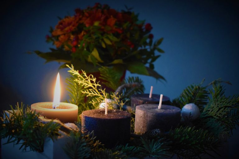 Advent: lit candles among evergreen branches and berries against a dark blue background